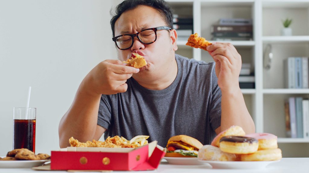 Asian fat man eating ultra-processed foods, hamburger, pizza, fried chicken