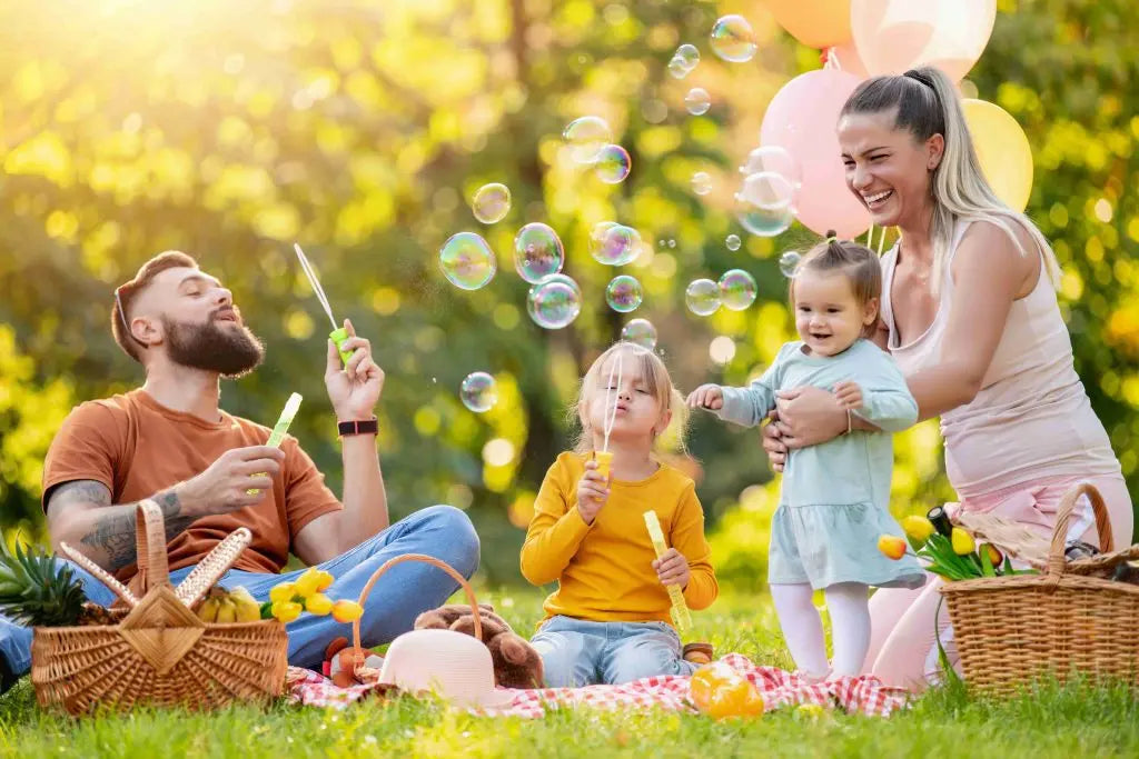 Happy family having spring outdoor fun picnic and blowing bubbles.