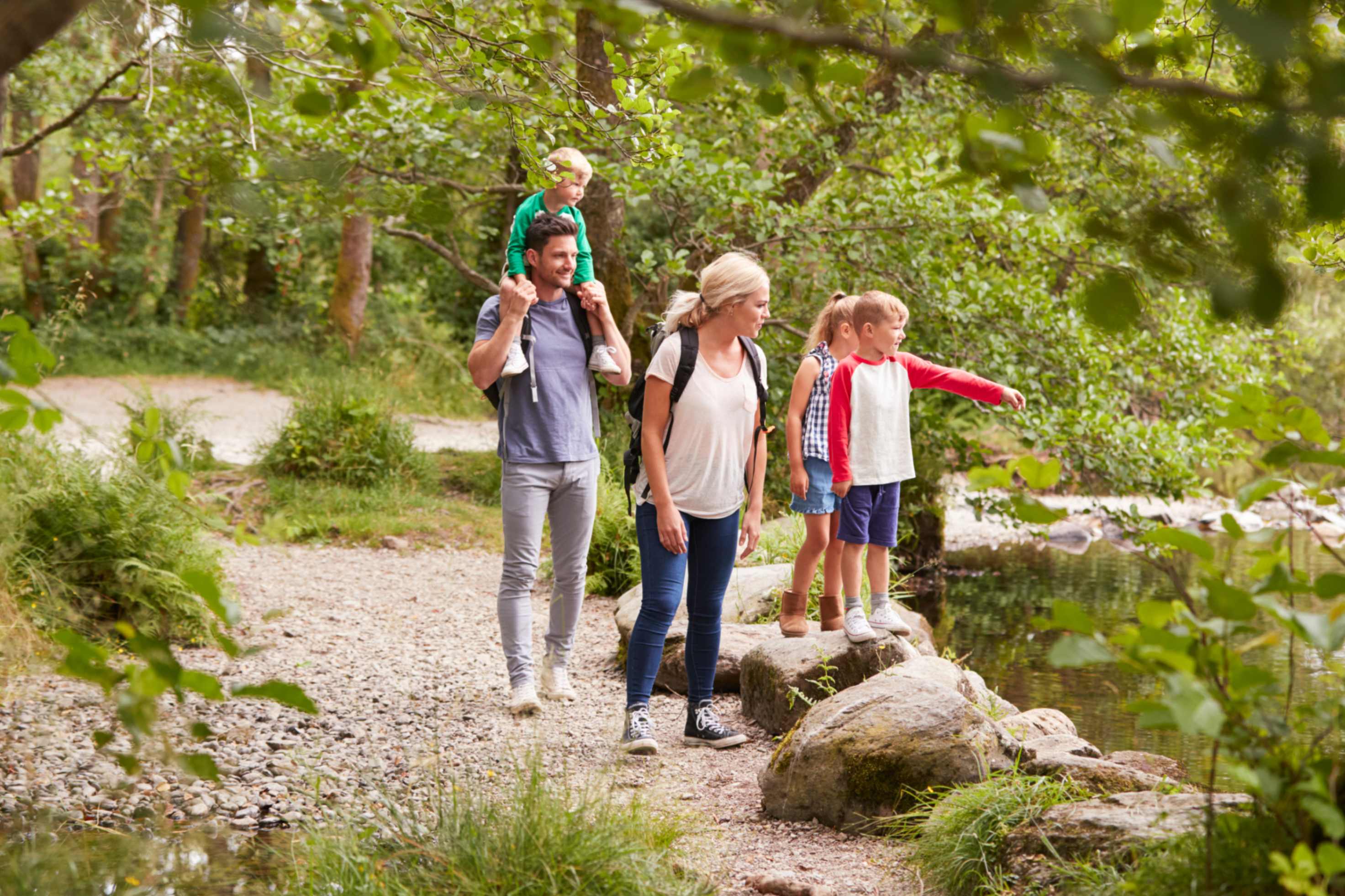 Family walking along path by river, spending time outdoors.