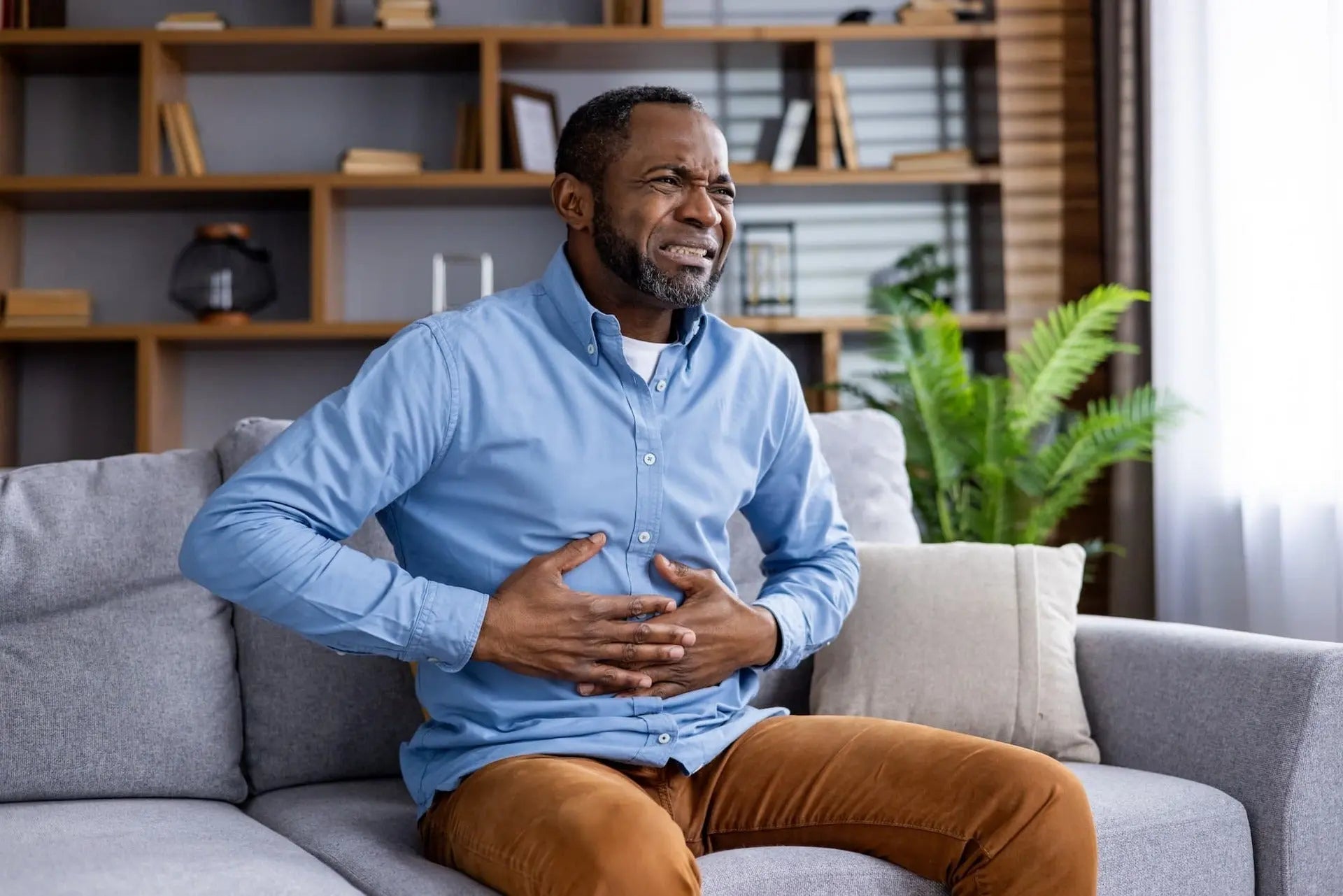 Man experiencing abdominal pain, a sign of Cyclospora symptoms, while seated on sofa in living room.